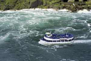 Maid of the Mist boat approaching the base of Niagara Falls with tourists in rain ponchos surrounded by mist